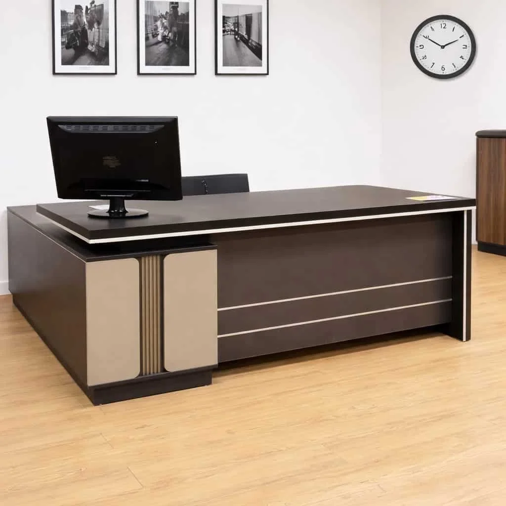 1600mm L-shaped executive desk in a dark espresso brown wood finish, featuring a floating-style desktop with slim silver trim accents, an attached side return storage credenza equipped with open shelving, a lockable drawer, and a sliding cabinet door, and a front modesty panel styled with contrasting beige geometric paneling and vertical slats.