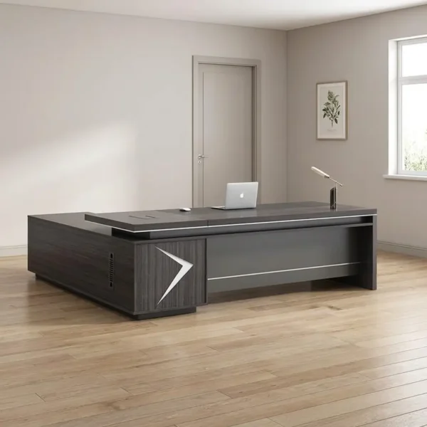 1.6m L-shaped executive table finished in a dark charcoal wood grain veneer, featuring a floating-style desktop with integrated metal trim accents, a large built-in side return credenza, a matte gray front modesty panel, and an illuminated chevron or arrowhead LED light inlay on the front support pedestal.