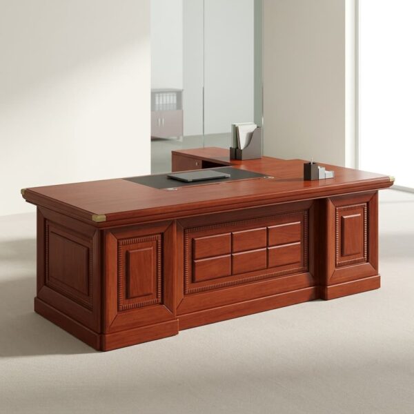 2.2M Executive L-Shaped Desk in a rich reddish-brown mahogany wood veneer finish, featuring a thick tabletop with brass corner guards, an integrated black leather desk blotter inlay, an attached side return credenza, and a traditional front modesty panel detailed with decorative recessed panels and a central grid-patterned carving.