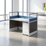 1 way office workstation shown from front and rear angles, featuring a spacious white tabletop with a built-in cable management grommet, a matching white under-desk three-drawer mobile filing cabinet with a key lock, and enclosing privacy partition panels styled with a brown lower section, a blue horizontal accent band, and clear glass top dividers set in a white frame.