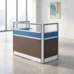 1 way office workstation shown from front and rear angles, featuring a spacious white tabletop with a built-in cable management grommet, a matching white under-desk three-drawer mobile filing cabinet with a key lock, and enclosing privacy partition panels styled with a brown lower section, a blue horizontal accent band, and clear glass top dividers set in a white frame.