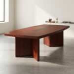 8-seater conference table featuring a long boat-shaped tabletop with a rich reddish-brown cherry wood veneer finish, a central black slatted cable management racetrack inlay, and a heavy-duty base consisting of thick slab legs and a solid rectangular pedestal base.