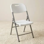 White foldable chair featuring a contoured molded white plastic seat and a matching backrest with an integrated cutout carrying handle, supported by a heavy-duty silver powder-coated tubular steel folding frame with black protective non-marring foot caps.