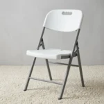 White foldable chair featuring a contoured molded white plastic seat and a matching backrest with an integrated cutout carrying handle, supported by a heavy-duty silver powder-coated tubular steel folding frame with black protective non-marring foot caps.