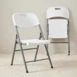 White foldable chair featuring a contoured molded white plastic seat and a matching backrest with an integrated cutout carrying handle, supported by a heavy-duty silver powder-coated tubular steel folding frame with black protective non-marring foot caps.