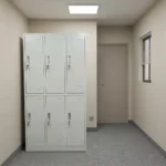 Light grey 6-door steel locker cabinet with recessed handles, individual key locks, and ventilation louvers next to an office desk.