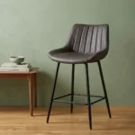Dark gray faux leather barstool with a ribbed vertical-tufted backrest and tapered black metal legs with a built-in footrest.