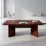 8-seater conference table featuring a long boat-shaped tabletop with a rich reddish-brown cherry wood veneer finish, a central black slatted cable management racetrack inlay, and a heavy-duty base consisting of thick slab legs and a solid rectangular pedestal base.