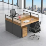 2 way office workstation arranged in a face-to-face configuration, featuring natural wood grain tabletops enclosed by charcoal gray privacy partition panels topped with frosted glass dividers, paired with a matching under-desk three-drawer mobile filing cabinet with lock.