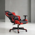 Ergonomic red gaming chair shown from front and side-profile reclined angles, featuring a high-back racing-style silhouette upholstered in black faux leather with vibrant red side panels, equipped with a removable neck pillow, an adjustable lumbar support cushion, T-shaped height-adjustable armrests, a reclining mechanism lever, and a matching five-star nylon swivel base on color-coordinated red-rimmed dual-wheel casters.