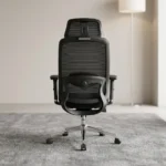 Orthopedic high-back office seat featuring a breathable black mesh backrest with an integrated adjustable lumbar support pad, a contoured black fabric-padded seat cushion, an independent wide mesh headrest, adjustable T-shaped armrests, a pneumatic lift lever, and a polished chrome five-star swivel base equipped with dual-wheel casters.