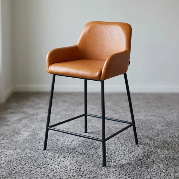 Brown leather counter barstool featuring a contoured bucket-style seat upholstered in tan or light brown faux leather with subtle textured grain, designed with low integrated armrests, a padded backrest, and slender matte black metal legs reinforced by a built-in square perimeter footrest.