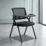 Foldable chair with writing pad featuring a breathable black mesh backrest, a thick padded black fabric seat cushion, a black metal folding scissor frame, and an integrated right-handed flip-up plastic tablet arm desk equipped with a built-in cup holder, anchored by short fixed armrests.