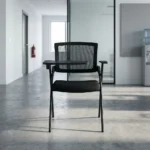 Foldable chair with writing pad featuring a breathable black mesh backrest, a thick padded black fabric seat cushion, a black metal folding scissor frame, and an integrated right-handed flip-up plastic tablet arm desk equipped with a built-in cup holder, anchored by short fixed armrests.