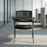 Foldable chair with writing pad featuring a breathable black mesh backrest, a thick padded black fabric seat cushion, a black metal folding scissor frame, and an integrated right-handed flip-up plastic tablet arm desk equipped with a built-in cup holder, anchored by short fixed armrests.