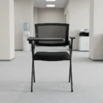 Foldable chair with writing pad featuring a breathable black mesh backrest, a thick padded black fabric seat cushion, a black metal folding scissor frame, and an integrated right-handed flip-up plastic tablet arm desk equipped with a built-in cup holder, anchored by short fixed armrests.