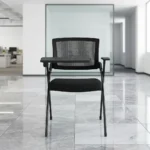 Foldable chair with writing pad featuring a breathable black mesh backrest, a thick padded black fabric seat cushion, a black metal folding scissor frame, and an integrated right-handed flip-up plastic tablet arm desk equipped with a built-in cup holder, anchored by short fixed armrests.