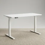 1.2m white electric desk featuring a clean rectangular desktop with rounded corners, dual circular white cable grommets, a black under-desk digital control keypad, and a height-adjustable white telescoping T-leg base.