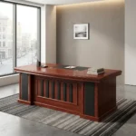 1.8m executive office desk featuring a rich, reddish-brown wood-grain finish, an integrated black writing pad inlay with dual grommet holes, a matching L-shaped side return cabinet, and a classic front modesty panel accented with vertical black inserts.