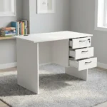 1.0m office study desk featuring a clean white finish, a circular black cable grommet on the tabletop, a matching modesty panel, and an integrated three-drawer pedestal with black curved handles and a lockable top drawer.