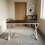 1.2m generic computer table featuring a sleek, rectangular black tabletop with a circular black cable grommet, supported by a modern geometric white metal X-frame leg base.