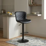 Black leather adjustable barstool featuring a curved bucket-style seat with diamond-quilted black leather upholstery, a matte black height-adjustable pedestal stand with a built-in oval footrest, and a matching circular trumpet base.