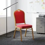 Red stackable banquet chair featuring a crown-back backrest with an integrated top carry handle, upholstered in vibrant red fabric with a subtle gold diamond lattice pattern, paired with a thick padded seat cushion and supported by a durable gold-finished metallic frame with protective bumper guards on the legs.