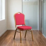 Red stackable banquet chair featuring a crown-back backrest with an integrated top carry handle, upholstered in vibrant red fabric with a subtle gold diamond lattice pattern, paired with a thick padded seat cushion and supported by a durable gold-finished metallic frame with protective bumper guards on the legs.