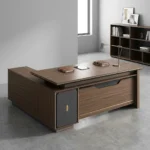 1.8m L-shaped office table featuring a premium dark wood-grain finish, an L-shaped configuration with an attached side return credenza, a thick floating-style tabletop, a front modesty panel accented by a thin gold horizontal line, and a unique gray side pedestal cabinet decorated with an "X" stitch pattern and a central gold accent tab.