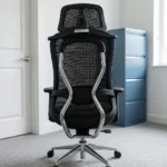 Ergonomic orthopedic office staff chair featuring a high-back design with an adjustable mesh headrest, a contoured black mesh backrest supported by an integrated skeletal lumbar structure, flat T-shaped adjustable armrests, a thickly cushioned black fabric seat, and a polished aluminum five-star swivel base on dual-wheel casters.