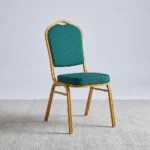 Stackable green banquet chair featuring a crown-top backrest and a thick square seat cushion, both upholstered in dark green fabric with a subtle gold fleck or dot pattern, supported by a sturdy gold-finished metallic frame with integrated stacking bumpers.