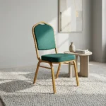 Stackable green banquet chair featuring a crown-top backrest and a thick square seat cushion, both upholstered in dark green fabric with a subtle gold fleck or dot pattern, supported by a sturdy gold-finished metallic frame with integrated stacking bumpers.