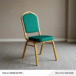Stackable green banquet chair featuring a crown-top backrest and a thick square seat cushion, both upholstered in dark green fabric with a subtle gold fleck or dot pattern, supported by a sturdy gold-finished metallic frame with integrated stacking bumpers.