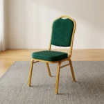 Stackable green banquet chair featuring a crown-top backrest and a thick square seat cushion, both upholstered in dark green fabric with a subtle gold fleck or dot pattern, supported by a sturdy gold-finished metallic frame with integrated stacking bumpers.
