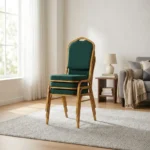 Green stackable banquet chair featuring a crown-top backrest with a cut-out handle and a thick square seat cushion, both upholstered in dark green fabric with a subtle gold dot or diamond pattern, shown in a vertical stack of three supported by a sturdy gold-finished metallic frame with white stacking bumpers.