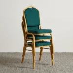 Green stackable banquet chair featuring a crown-top backrest with a cut-out handle and a thick square seat cushion, both upholstered in dark green fabric with a subtle gold dot or diamond pattern, shown in a vertical stack of three supported by a sturdy gold-finished metallic frame with white stacking bumpers.