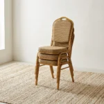 Stackable brown conference chair featuring a crown-top backrest with a cut-out handle and a thick square seat cushion, both upholstered in a textured light-brown or beige patterned fabric, shown in a vertical stack of three supported by a sturdy gold-finished metallic frame with integrated stacking bumpers.