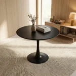 Modern black dining table featuring a sleek tulip-style design with a smooth matte-black circular tabletop, supported by a central tapered pedestal stem that flares out into a matching wide circular base.