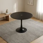 Modern black dining table featuring a sleek tulip-style design with a smooth matte-black circular tabletop, supported by a central tapered pedestal stem that flares out into a matching wide circular base.