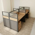4-way modular workstation featuring four light oak-finish desks arranged in a 2x2 cluster, separated by semi-private partition screens with dark gray lower panels, light oak accent trim, and frosted glass upper sections, complete with individual under-desk three-drawer mobile pedestals and integrated desktop cable grommets.