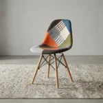 Modern patchwork Eames-style chair featuring a contoured shell seat upholstered in a multi-patterned fabric blend of houndstooth, plaid, and solid earthy tones, supported by natural wood dowel legs with black metal Eiffel-style wire bracing.