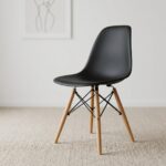 Black Eames-style dining chair featuring a molded matte black polypropylene shell seat, supported by natural wood dowel legs with black metal Eiffel-style wire bracing.