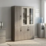 3-door wooden executive cabinet featuring a two-tone finish with taupe wood-grain laminate, upper cream-framed glass display doors revealing internal shelving, lower solid wooden doors, modern dark vertical handles, and key-lock security mechanisms.