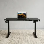 Black electric adjustable standing desk featuring a textured carbon-fiber tabletop, a digital LED control panel with memory presets, an integrated cup holder and headphone hook, cable management grommets, and a sturdy matte black T-frame steel base.