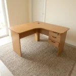 1.4m L-shaped office desk featuring a light oak wood-grain laminate finish, a curved corner desktop with an integrated cable grommet, wooden modesty panels, and an attached right-hand 3-drawer storage pedestal with dark curved handles and a key lock.