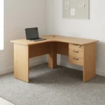 1.4m L-shaped office desk featuring a light oak wood-grain laminate finish, a curved corner desktop with an integrated cable grommet, wooden modesty panels, and an attached right-hand 3-drawer storage pedestal with dark curved handles and a key lock.