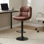 Brown leather adjustable barstool featuring a plush, tufted warm brown leatherette seat and backrest, supported by a matte black pedestal stem, an integrated circular footrest, pneumatic gas-lift height adjustment, and a round matte black base.