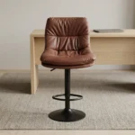 Brown leather adjustable barstool featuring a plush, tufted warm brown leatherette seat and backrest, supported by a matte black pedestal stem, an integrated circular footrest, pneumatic gas-lift height adjustment, and a round matte black base.