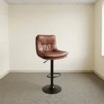 Brown leather adjustable barstool featuring a plush, tufted warm brown leatherette seat and backrest, supported by a matte black pedestal stem, an integrated circular footrest, pneumatic gas-lift height adjustment, and a round matte black base.