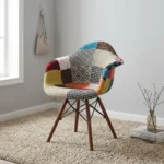 Eames-style patchwork armchair featuring a molded shell seat upholstered in vibrant multi-patterned fabric patchwork with integrated curved armrests, supported by dark wood legs and black metal Eiffel wire bracing.